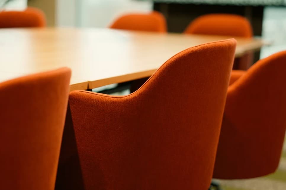 Sala de juntas con sillas color naranja alrededor de una mesa de madera